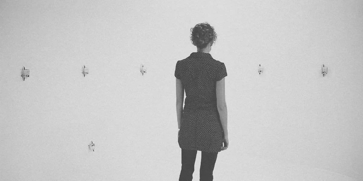 Woman standing in the centre of an empty room with blank white walls and surrounded by small cameras.