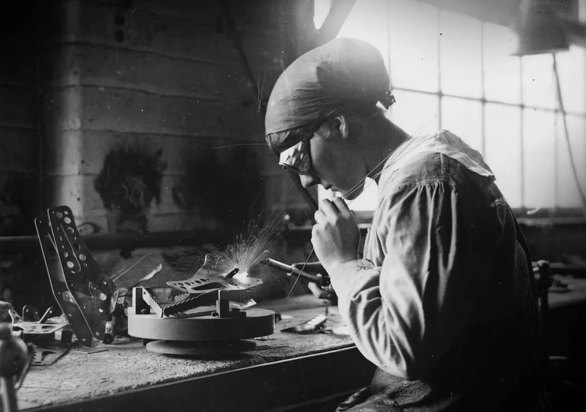 Vintage black and white photo of a woman welding metal components together.